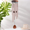 Carillon suspendu en tubes d'aluminium rose gold et en bois, exposé sur un fond lumineux.