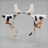 A headband featuring cow ears made of light beige faux fur, decorated with black and white cow print fabric and a ribbon bow.