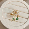 A gold cocktail ring featuring a floral design with clear stones and two green leaf accents.