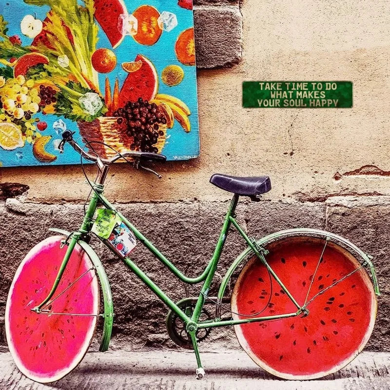 A vintage green bicycle with a watermelon-themed paint job is parked against a textured wall next to a sign.