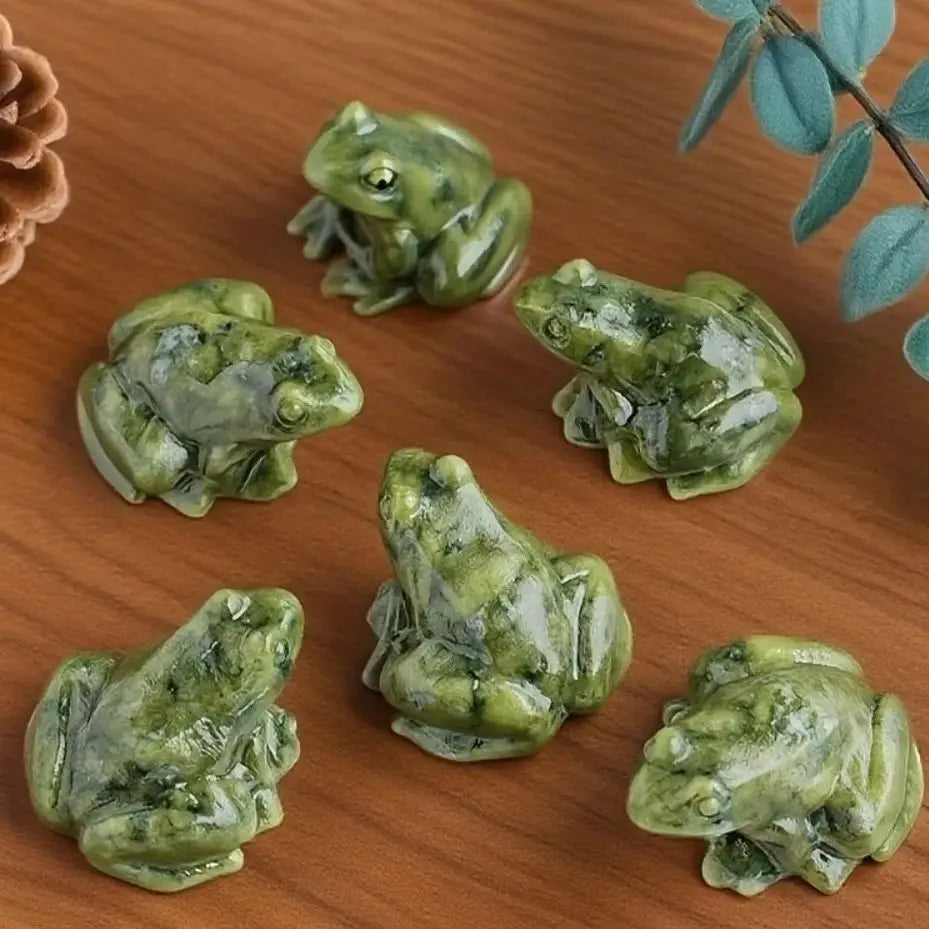 Petite figurine de grenouille de jade verte, miniature, posée sur une surface en bois.