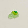 A small, translucent green resin charm shaped like a fruit turtle with a green top and a black eye.