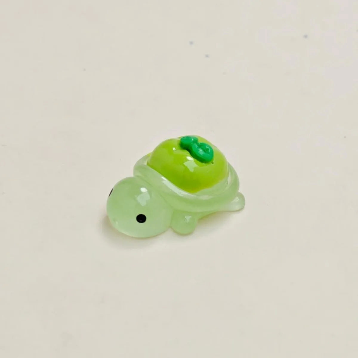 A small, translucent green resin charm shaped like a fruit turtle with a green top and a black eye.