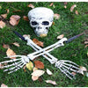 A realistic white skeleton arm stake lying on green grass with fallen autumn leaves.