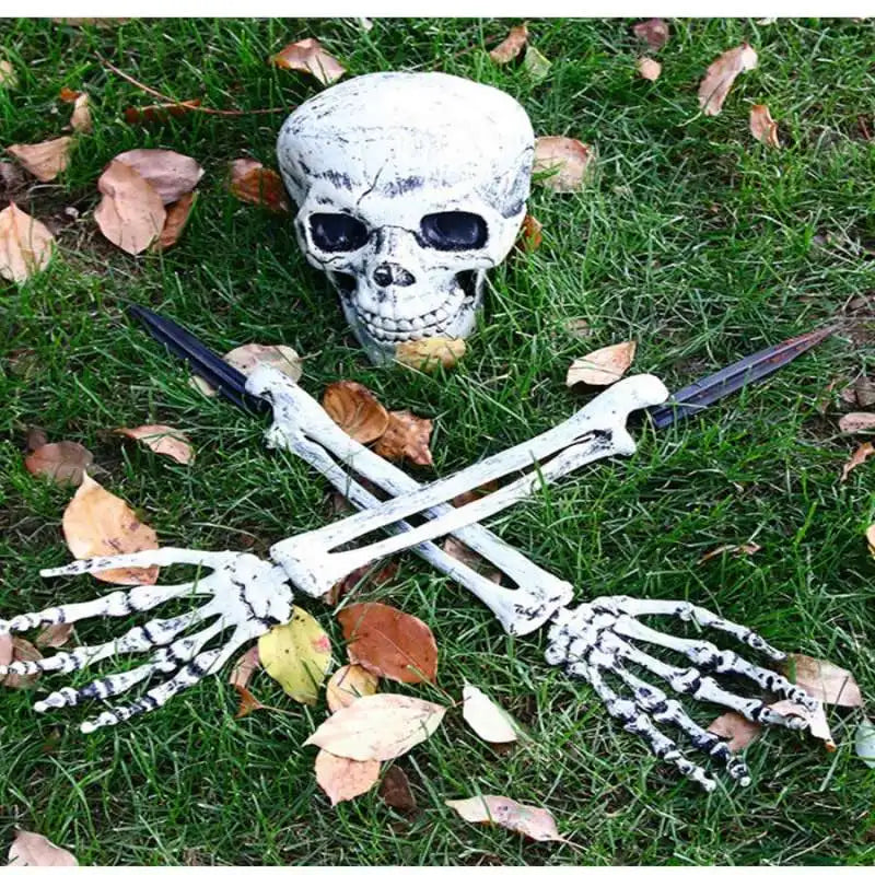 A realistic white skeleton arm stake lying on green grass with fallen autumn leaves.