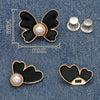A set of black butterfly waist tightener buttons with pearl accents shown against a denim background.