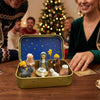 A hand-painted mini nativity set featuring figures in a gold tin storage box on a wooden table.