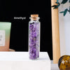 A glass bottle filled with amethyst crystals resting on a white surface.