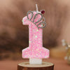 A pink glitter birthday candle shaped like the number one with a silver crown topper.