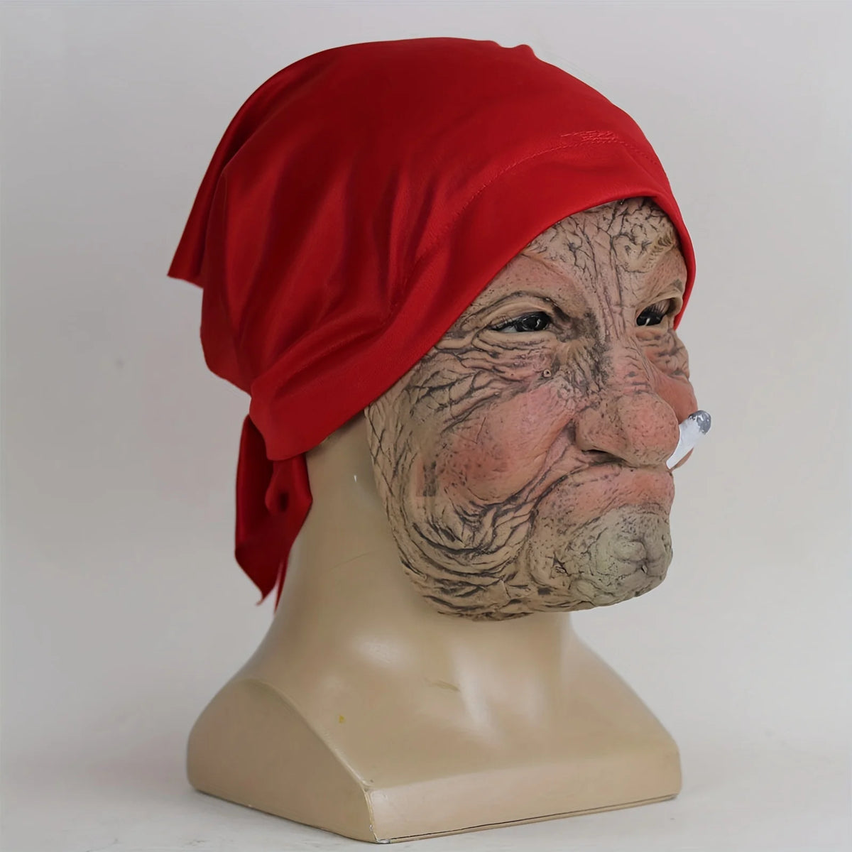 A realistic latex horror mask of an elderly woman with wrinkled skin and red head covering displayed on a mannequin.