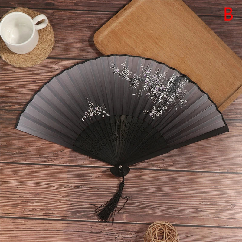 A dark gray lace folding hand fan with delicate white floral embroidery rests on a wooden surface next to a cup and a straw m