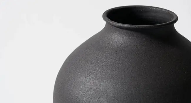 A close-up view of a large matte black decorative vase with a wide mouth and rounded body.