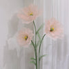 A large artificial silk pink poppy flower with green stem displayed in a stand against a white background.
