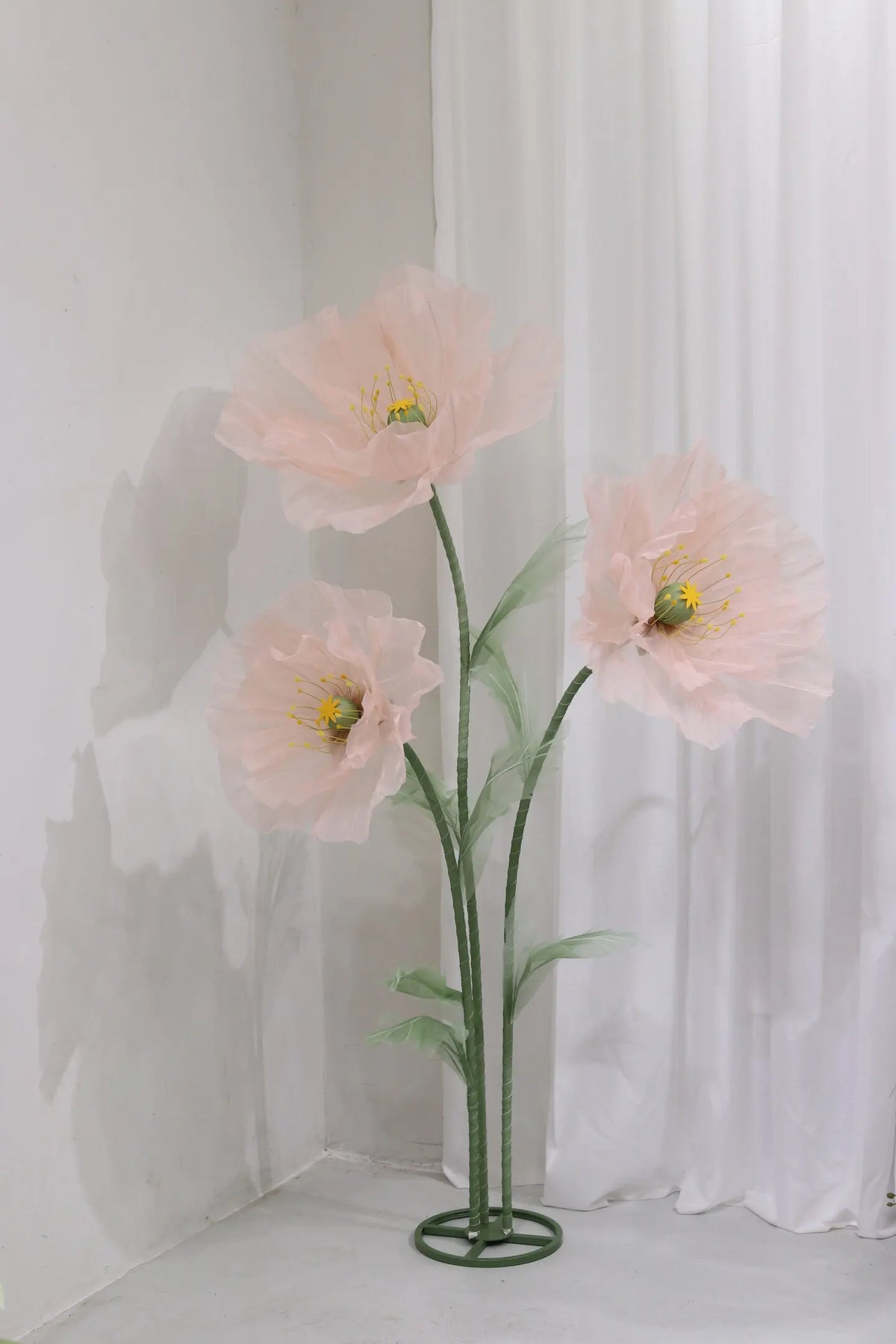A large artificial silk pink poppy flower with green stem displayed in a stand against a white background.