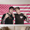 A man in a black shirt and a woman in a black shirt pose in front of an American flag tapestry wall art.