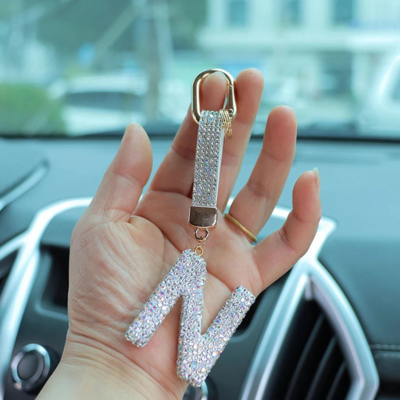 A hand holds a crystal letter keychain charm shaped like the letter N.