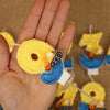 A hand holds a yellow construction excavator birthday cake candle for kids against a brown background.