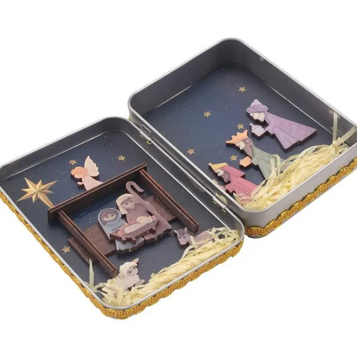 A rectangular tin box containing a hand-painted nativity scene decoration with figures and straw details.
