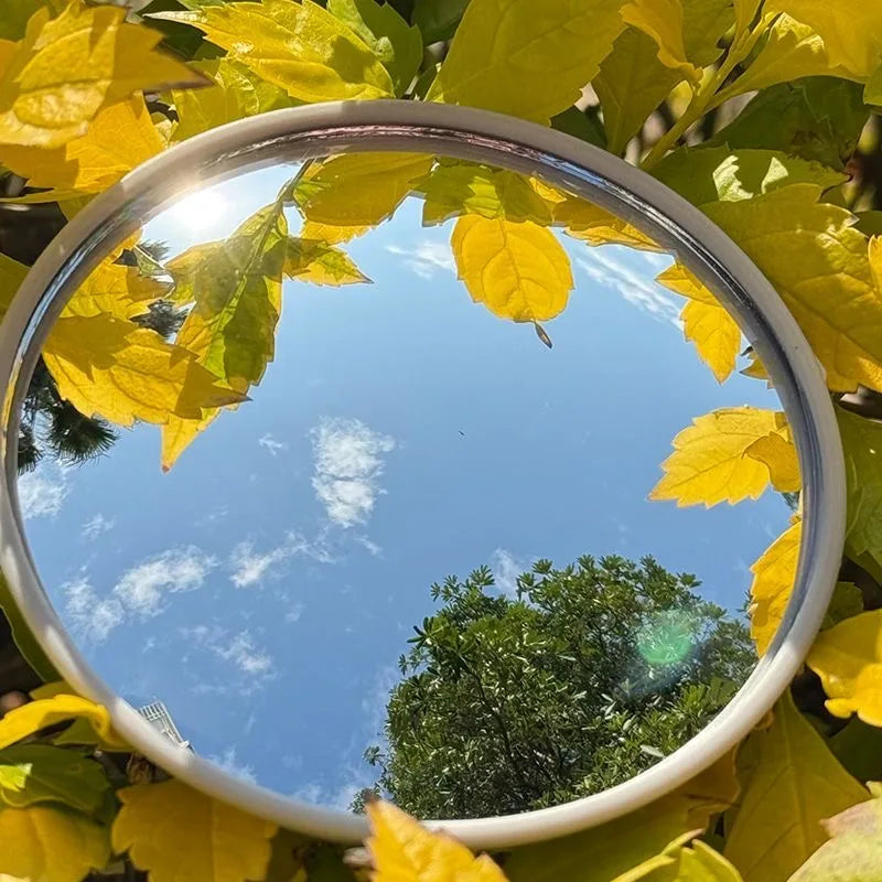 Eine kreisförmige konvexe Spiegel reflektiert einen hellblauen Himmel und grünes Laub.
