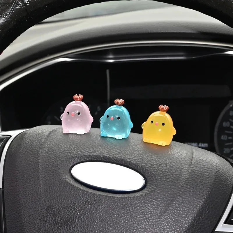 Three luminous resin chicken car ornaments in pink, blue, and yellow resting on a car dashboard.