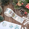 Roll of glittery laser Christmas snowflake stickers on a wooden surface with pine branches and greenery