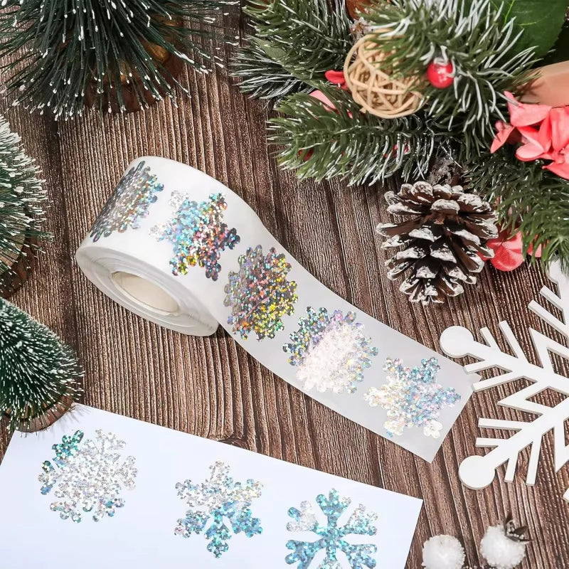Roll of glittery laser Christmas snowflake stickers on a wooden surface with pine branches and greenery
