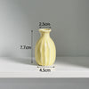 A light yellow ceramic mini vase with vertical ridges, shown against a gray background.