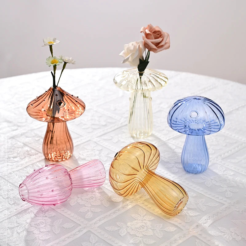 Collection de vases en forme de champignons en verre de couleurs rose, blanc et bleu, exposés sur une nappe en dentelle blanc