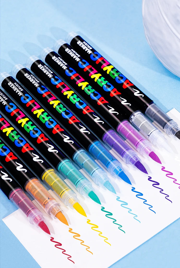 A set of 36 black acrylic paint markers with various colored tips lying on a white sheet of paper.