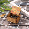 A wooden hand crank music box with an orange and yellow sun design resting on a white frame.