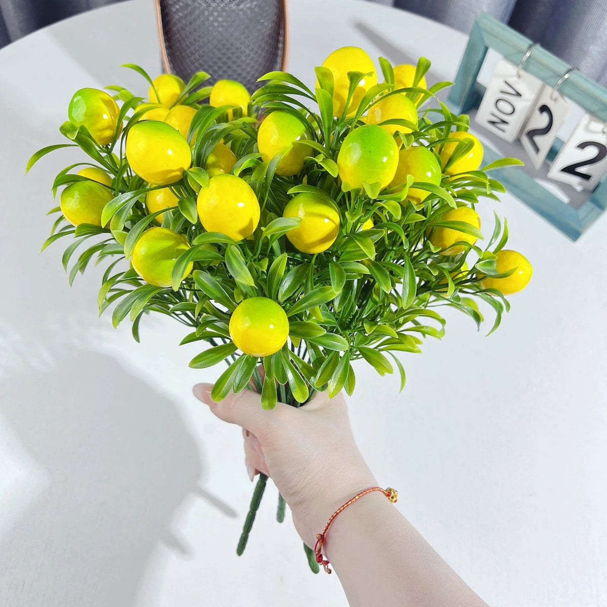 A hand holds a bouquet of bright yellow artificial lemon branch stems for decoration.