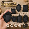 A hand holds several black resin floating sculpture photo frames with ornate edges on a textured background.