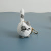 A handcrafted crochet cat keychain pendant with gray and white fur resting on a smooth blue-gray surface.