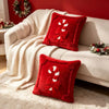 A red candy cane shaped Christmas pillow cover resting on a white sofa with a cream blanket and festive greenery.