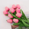 A bouquet of pink tulips with green leaves arranged on a white surface.
