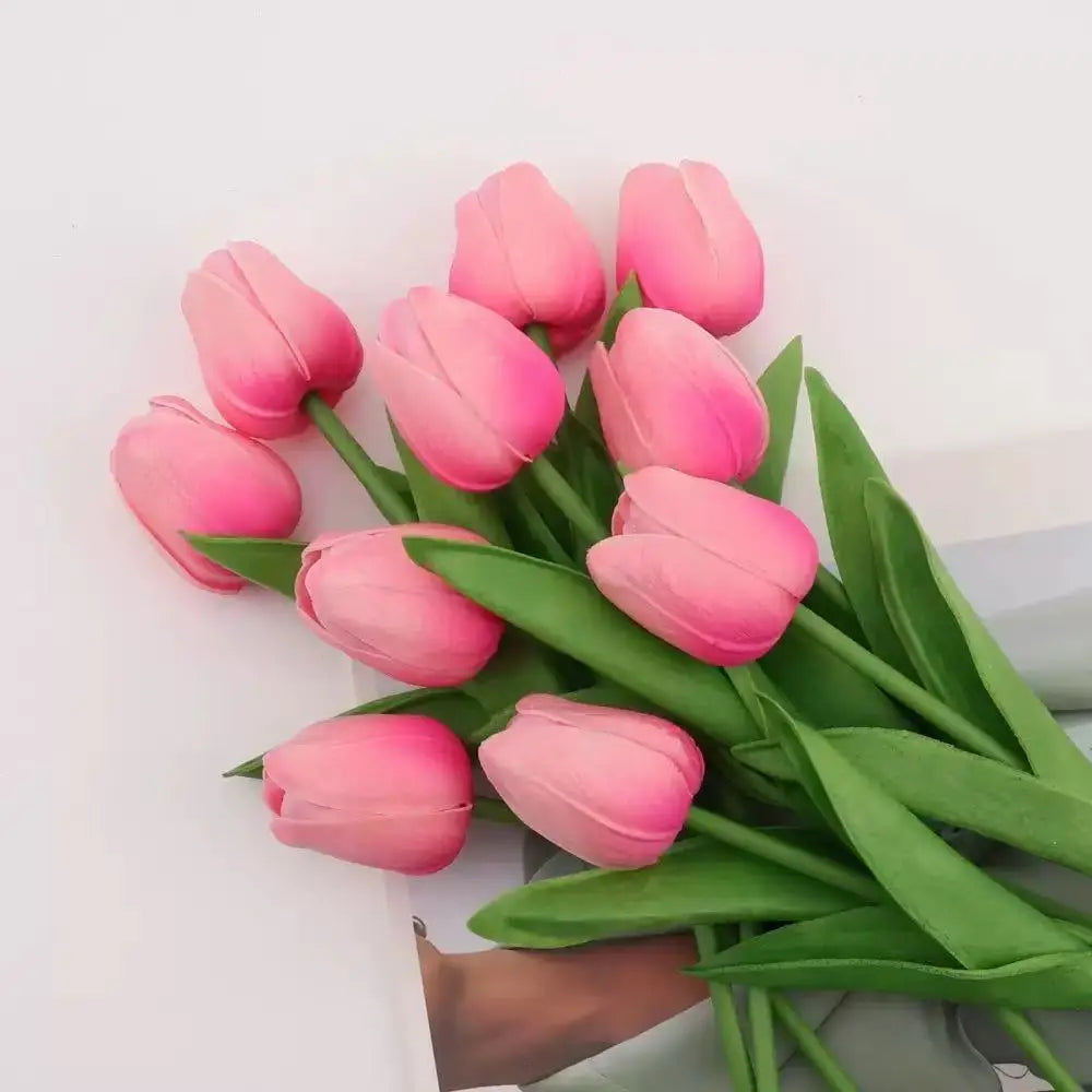 A bouquet of pink tulips with green leaves arranged on a white surface.