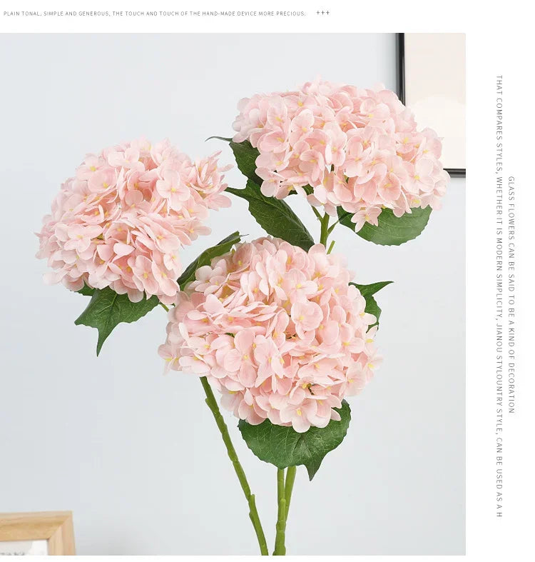 A bouquet of pink artificial hydrangeas with green leaves displayed against a light gray background.