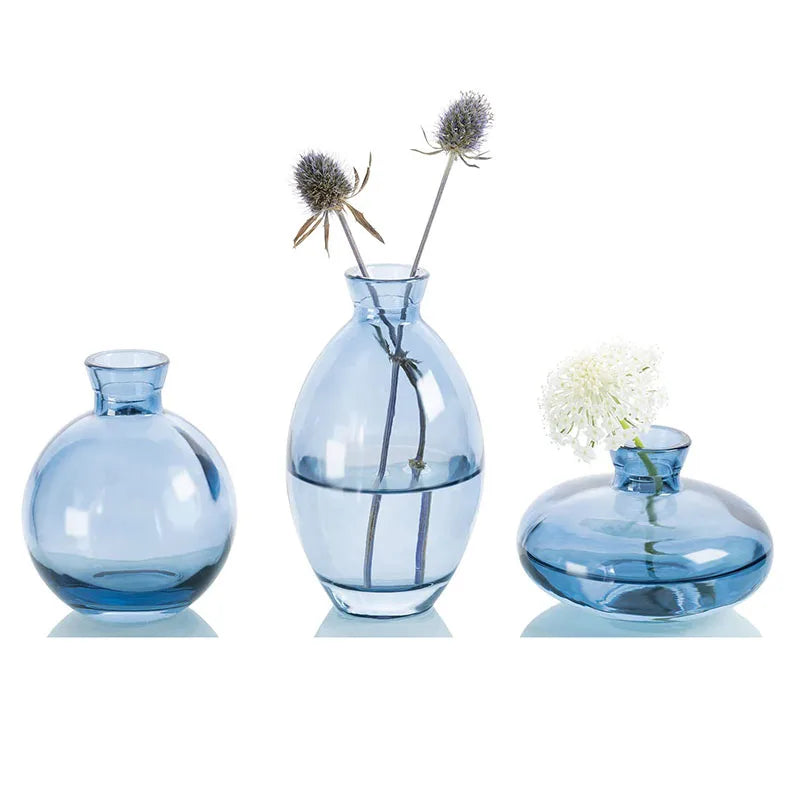 A set of three minimalist glass bud vases in varying sizes and shades of blue, with dried floral stems.