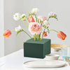 A bouquet of pink and white flowers arranged in a dark green block for party decor.