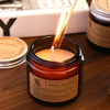 A hand-poured soy aromatherapy candle in a glass jar with a lit wick, set on a wooden surface.