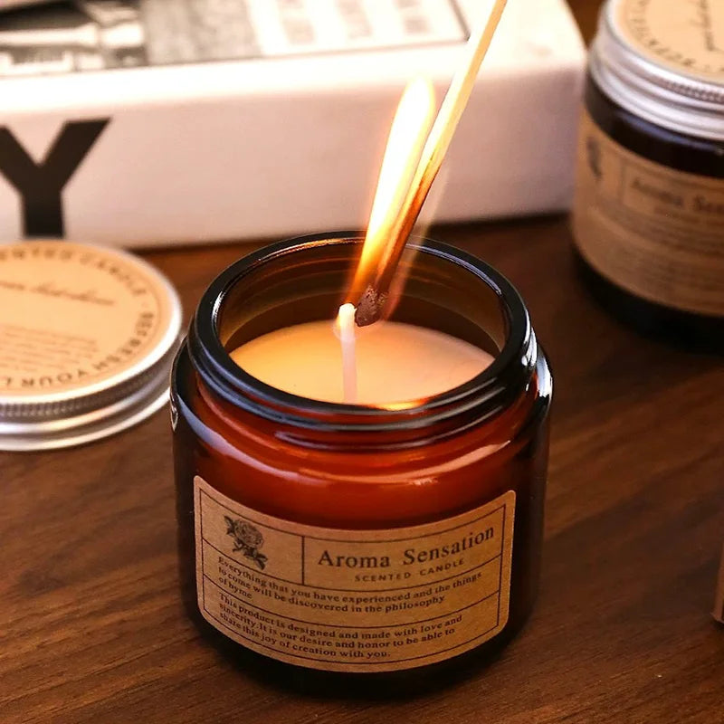 A hand-poured soy aromatherapy candle in a glass jar with a lit wick, set on a wooden surface.
