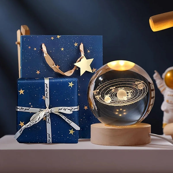 A blue gift box decorated with gold stars and a star, next to a glass crystal ball night light on a wooden base.