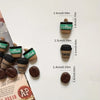 A collection of coffee bean fridge magnets in various shades and sizes displayed on a white surface.