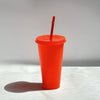 An orange glitter party cup with a red lid and straw standing on a white surface.
