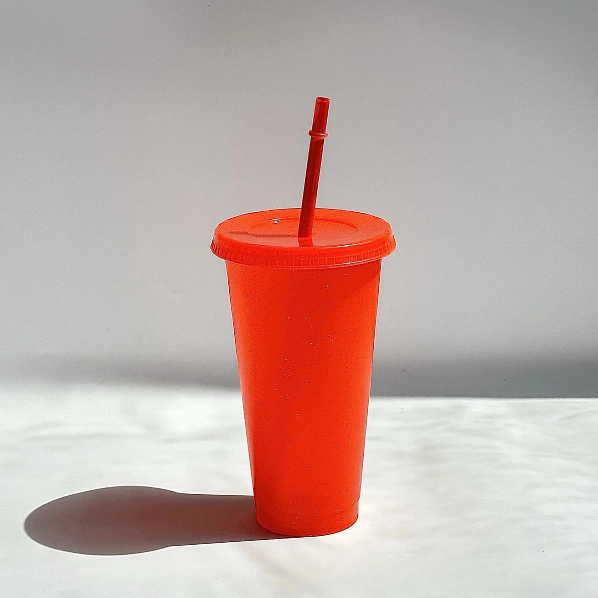 An orange glitter party cup with a red lid and straw standing on a white surface.