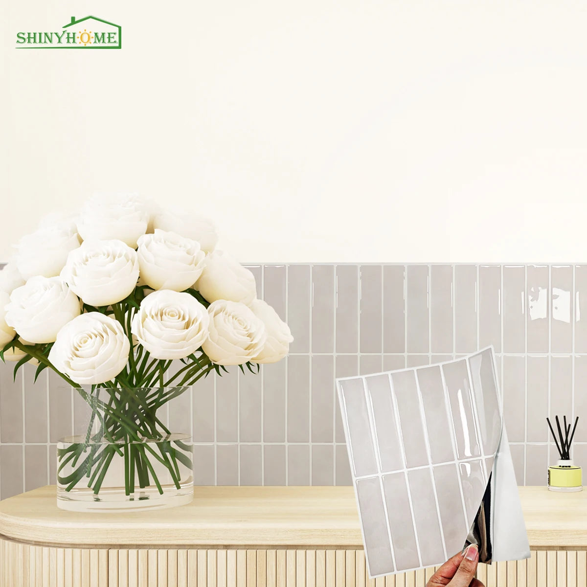 A bouquet of white roses displayed in a glass vase next to a display of self-adhesive heat resistant wall tiles.
