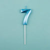 A blue birthday candle shaped like the number seven on a white stick against a light teal background.