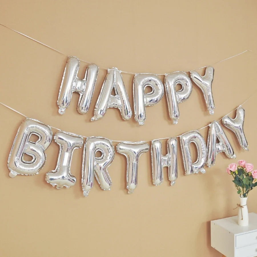 Silver foil letter balloons spelling out Happy Birthday strung across a beige wall for party decoration