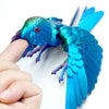 A hand holds a vibrant blue parrot figurine with movable wings.