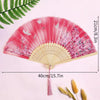 A pink and magenta folding fan with delicate floral patterns and a tassel, shown against a light pink background.